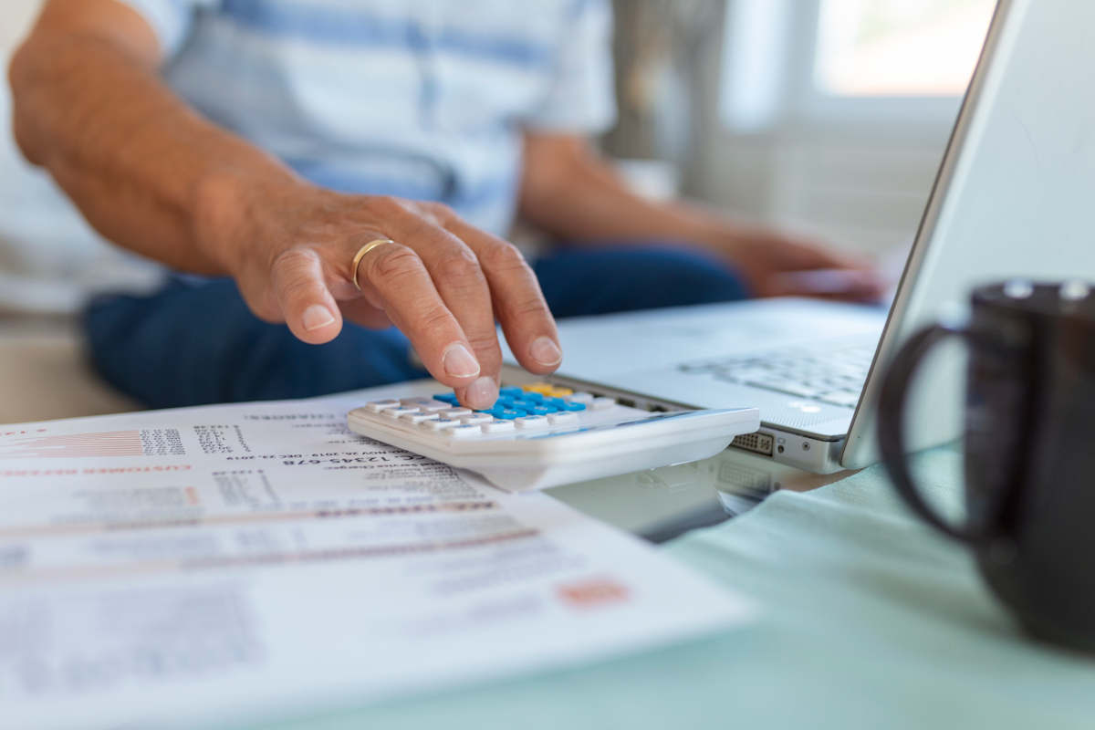 Pessoa fazendo contabilidade com caderno, calculadora e comprovantes fiscais organizados na mesa